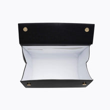 An overhead view of a structured large black handbag with the top flap held fully open, revealing the empty white insulated interior lining and the gold magnetic closures on the flap.