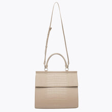 A front-facing studio shot of the light beige top-handle handbag, featuring a crocodile-embossed texture on the body and flap. The bag is shown hanging from its thin, adjustable shoulder strap, with the top handle and gold hardware visible.
